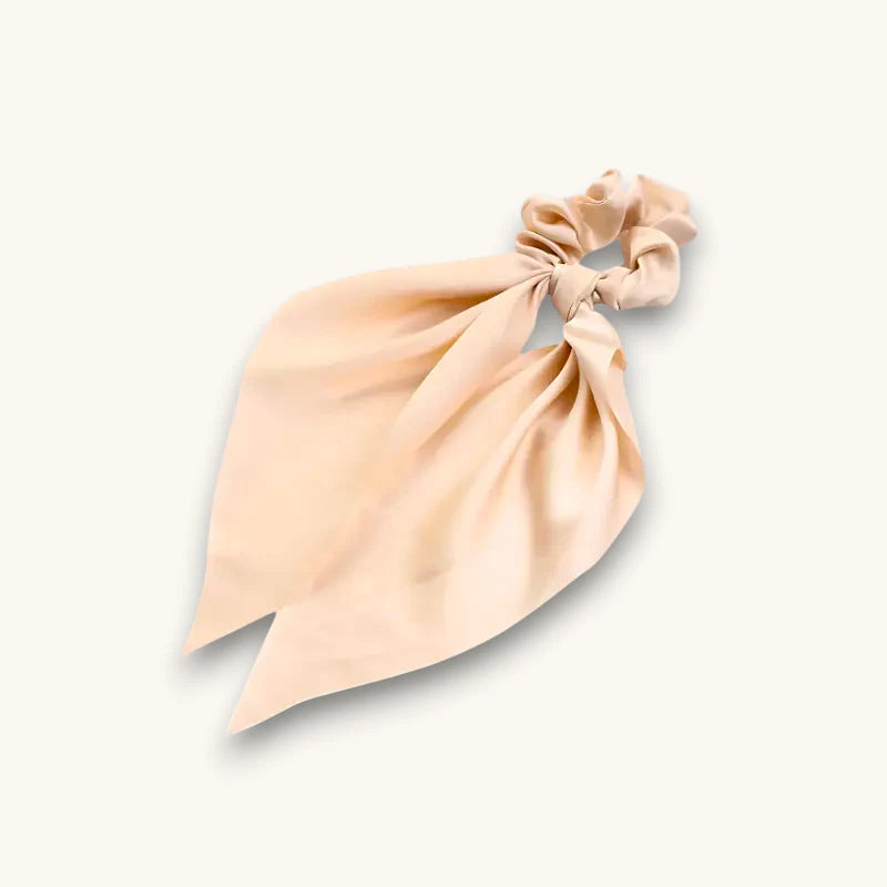 Soft blush pink satin scrunchie with flowing tied ribbon tail on beige scarf