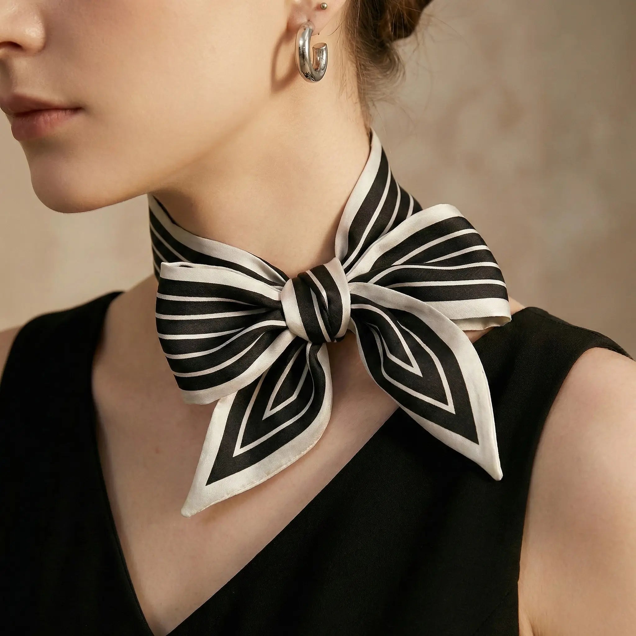 A woman wearing an elegant black and white striped silk neck scarf tied in a bow from Scarf Maison. Image