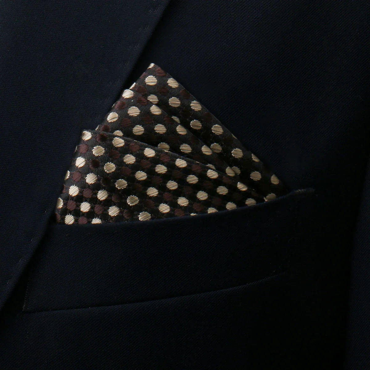 Brown pocket square with gold and beige polka dots in black suit pocket