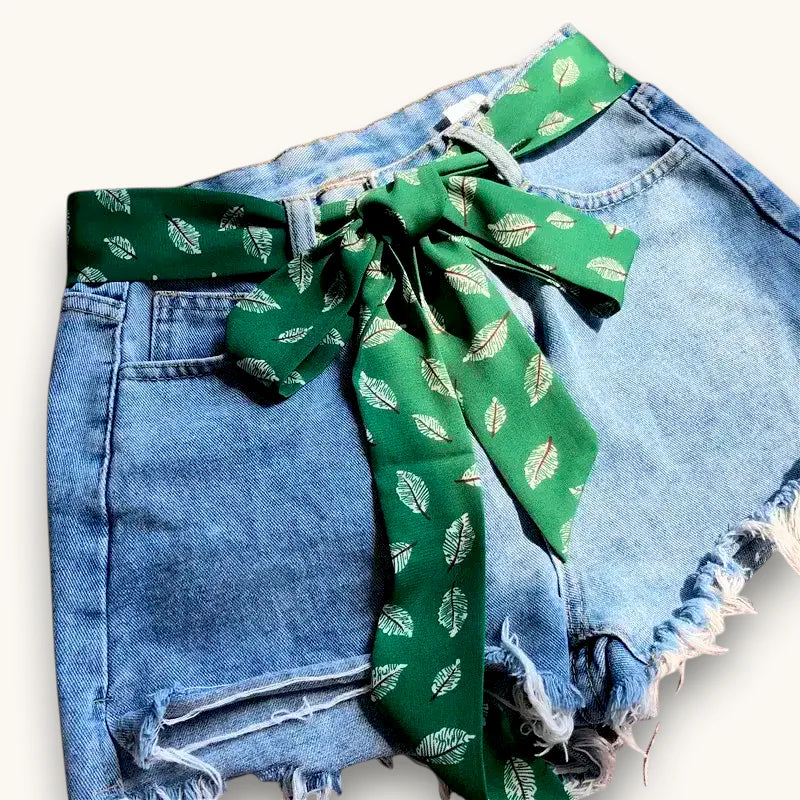Green scarf belt with leaf pattern tied in bow on denim shorts