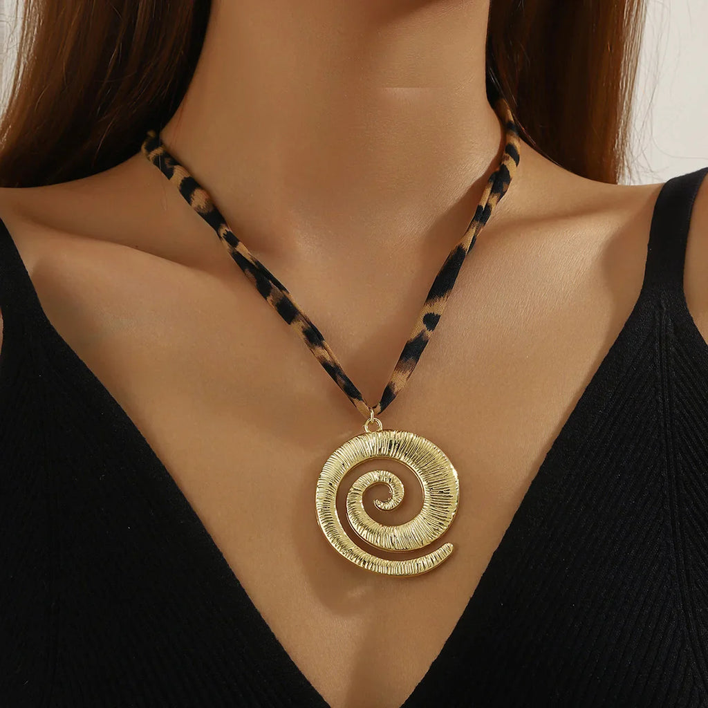 Gold-toned spiral pendant necklace with leopard-print cord on maroon scarf