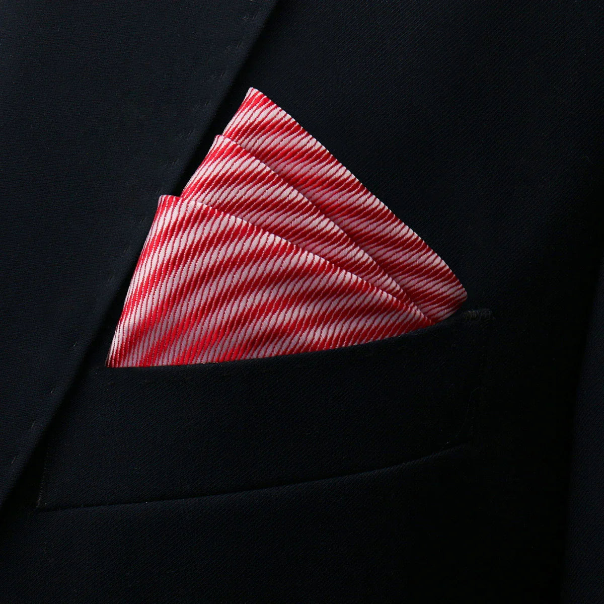Red pocket square with vibrant red-white diagonal stripes in black suit pocket