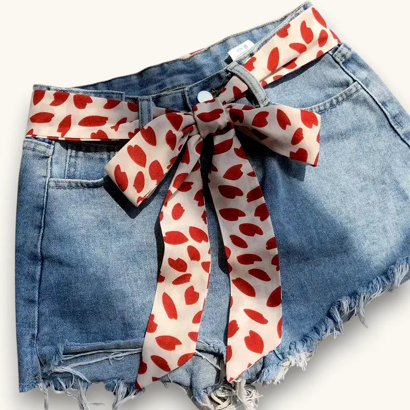Red scarf belt with heart pattern tied in bow on denim shorts waist