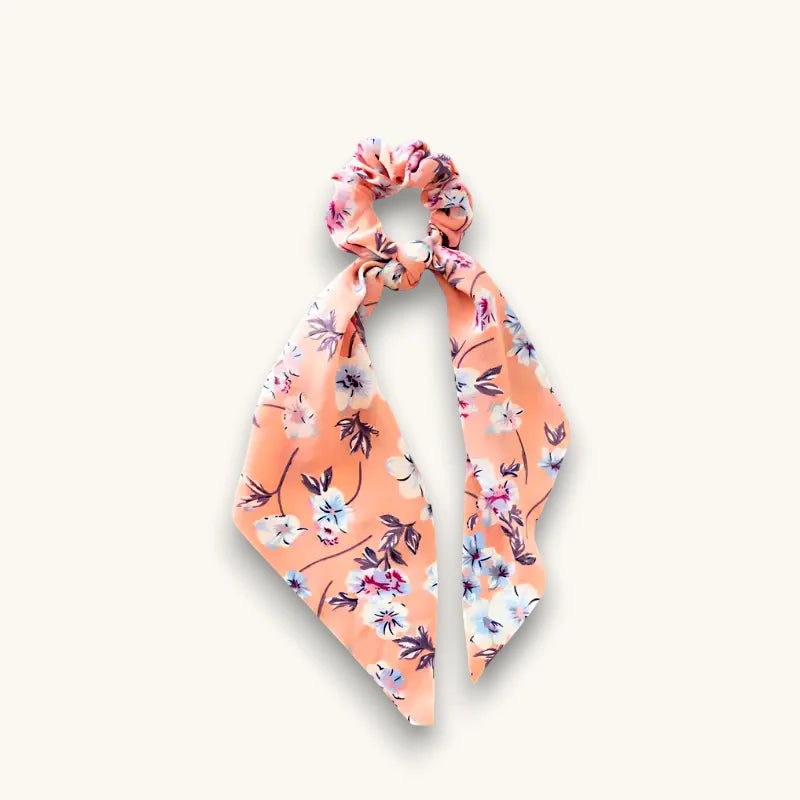 Peach satin bow scrunchie with delicate floral pattern in pinks, blues, purples